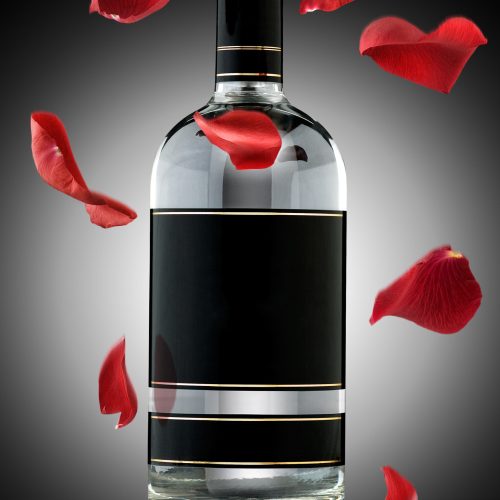 A photo of luxury alcohol bottle with falling rose leaves.